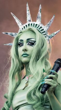 a woman dressed as the statue of liberty holding a microphone in her hand and wearing green makeup