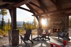 a covered patio with chairs and fire place in the background, overlooking trees and mountains