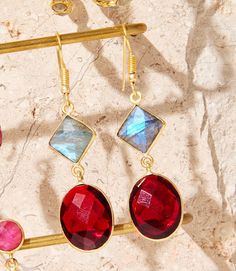 Elevate your jewelry collection with our Muti Gemstone Earrings. The striking combination of garnet and labradorite, set in a luxurious gold setting, will catch anyone's eye. These earrings are the perfect addition to any outfit, adding a touch of elegance and sophistication. Material: Brass gold plated, labradorite, glass Dimensions: 2.5" Weight: 0.30 oz. Imported Brass Gold, Gemstone Earrings, Stocking Stuffers, Labradorite, Garnet, Jewelry Collection, Gold Plate, Plating, Brass