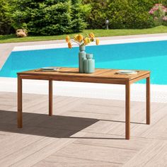 a wooden table sitting next to a swimming pool with flowers in vases on it