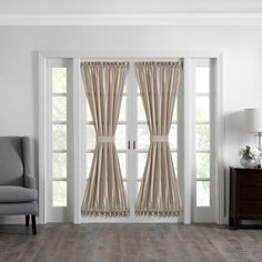 a living room with white walls and wooden flooring, two windows covered in beige drapes