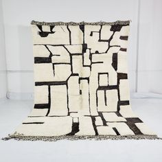 a black and white area rug with fringes on the bottom, in front of a white wall