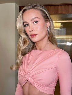 a woman with blonde hair wearing a pink top and posing in front of a mirror