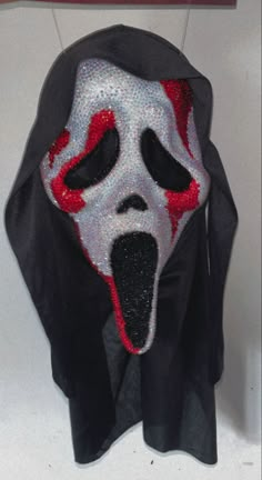 a mask with red and white paint on it's face is hanging from the wall