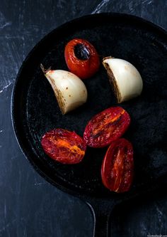 sliced tomatoes and onions in a cast iron skillet on a black surface with dark background