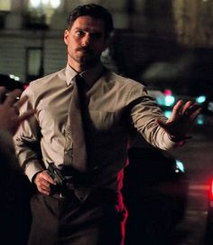 a man in a suit and tie standing on the street with his hands out to someone