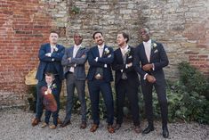 a group of men standing next to each other in front of a brick wall with their arms crossed