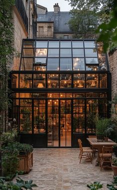 an outdoor dining area with tables and chairs in front of a glass walled building at dusk