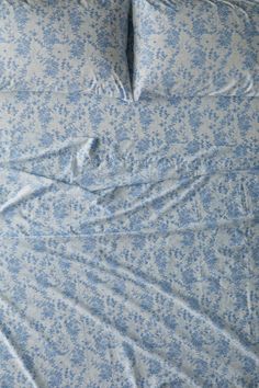 an unmade bed with blue and white floral print on the comforter, sheets and pillowcases