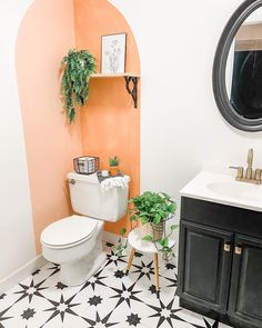 a white toilet sitting next to a sink in a bathroom under a mirror and potted plant