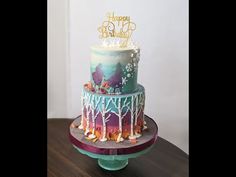 a three tiered cake with colorful frosting and trees on the top is sitting on a table in front of a white wall