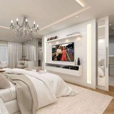 a white bedroom with chandelier and large television on the wall above the bed