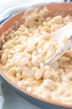 a wooden spoon stirring macaroni and cheese in a skillet on a table