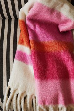 a pink and orange striped blanket sitting on top of a couch next to a pillow