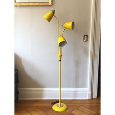 a yellow floor lamp with three lamps on it in front of a white wall and wooden floors