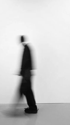 a blurry image of a man in a suit and hat walking past a white wall