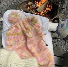 someone is knitting in front of a campfire with their feet propped up on the blanket