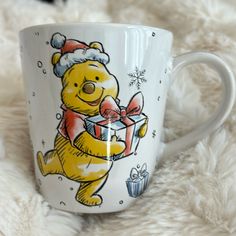 a winnie the pooh coffee mug with a christmas present in its mouth on a fluffy white blanket