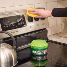 a person is cleaning the stove with a sponge and a bottle of green stuff next to it