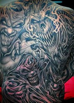 the back of a man's shoulder with tattoos on it and two faces in different colors