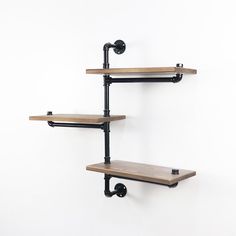 three wooden shelves with black metal brackets and wheels on each shelf, against a white wall