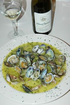 a white plate topped with clams next to a bottle of wine