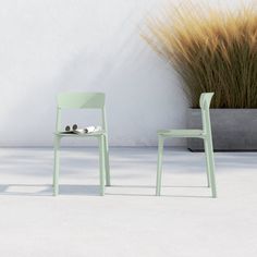 two green chairs sitting next to each other near a planter with grass in it