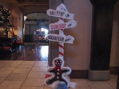 a pole with street signs on it in the middle of a hallway next to a christmas tree