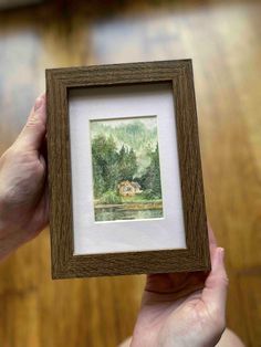 a person holding up a wooden frame with a painting on it