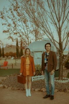 a man and woman standing next to each other in front of a house with trees