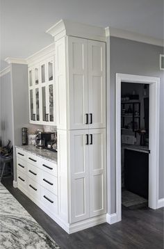 a kitchen with white cabinets and marble counter tops