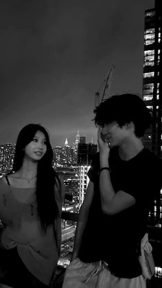 two young people standing next to each other in front of a cityscape at night