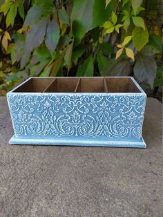 a blue planter sitting on top of a cement surface next to green leaves and bushes