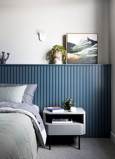 a bed sitting next to a night stand with a painting on the wall above it