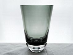 an empty glass sitting on top of a gray tableclothed surface with a white wall in the background