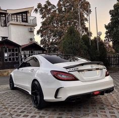 the rear end of a white car parked in front of a house