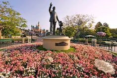 the statue is surrounded by pink flowers in front of disney's castle at disneyland world