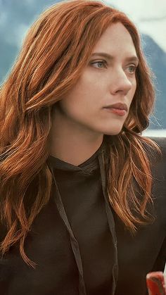 a woman with long red hair sitting in a chair looking off into the distance and wearing a black shirt