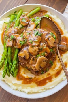 a white plate topped with mashed potatoes covered in mushrooms and gravy next to asparagus