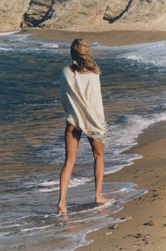 a woman standing on top of a sandy beach next to the ocean under a blanket