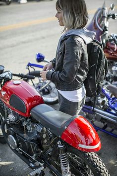 a woman standing next to a red and black motorcycle