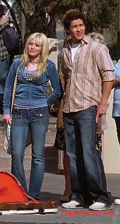 a man and woman standing next to each other on the street with people behind them