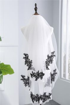 a white and black wedding veil hanging from a hook in a room with a potted plant