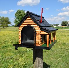 a small log house with a black roof and chimney is on a post in the grass