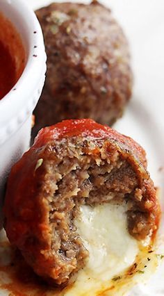 some meatballs and sauce on a white plate with a cup of tomato soup in the background