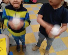 two young children are playing with a ball in a room full of other kids and one boy is holding something