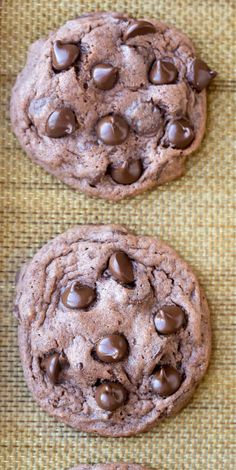 two chocolate chip cookies sitting on top of a brown table cloth next to each other