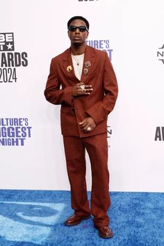 a man in a suit and sunglasses standing on a blue carpet