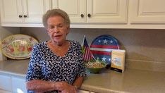 an older woman standing in front of a counter with plates and bowls on top of it