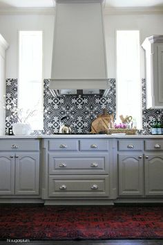 a kitchen with white cabinets and black tile on the backsplash, along with a red area rug